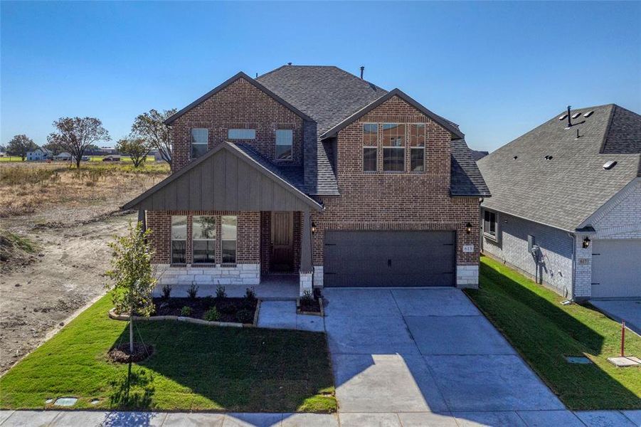 View of front of property featuring brick siding, a front yard, driveway, and roof with shingles
