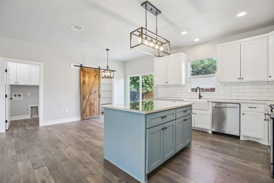 Kitchen with a barn door, white cabinetry, stainless steel appliances, dark wood finished floors, and recessed lighting