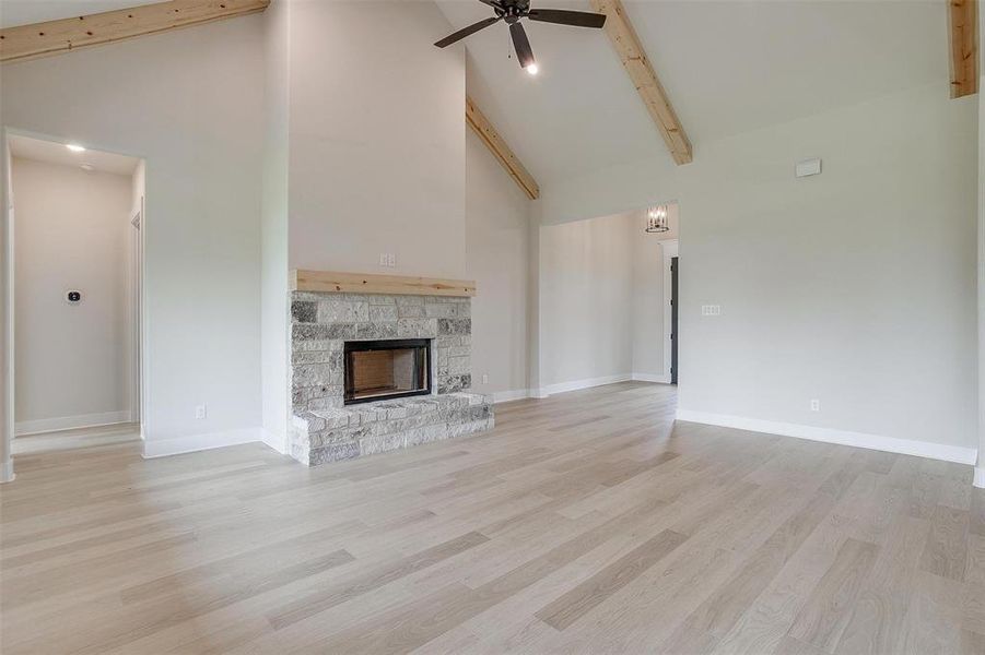 Unfurnished living room with ceiling fan, light hardwood / wood-style flooring, beam ceiling, a fireplace, and high vaulted ceiling