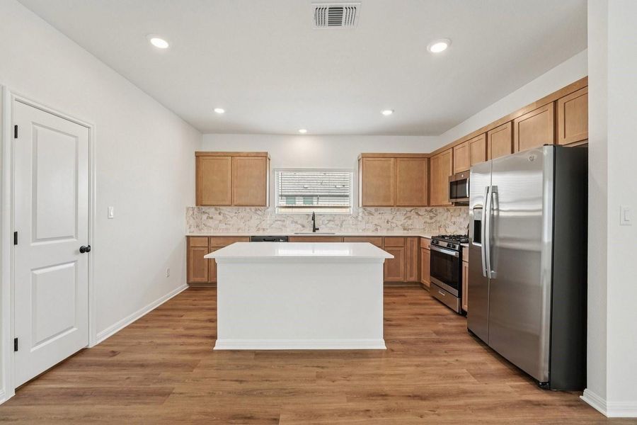 A pristine kitchen features a large central island, light wood cabinetry, and sleek stainless steel appliances. A pristine kitchen features a large central island, light wood cabinetry, and sleek stainless steel appliances.