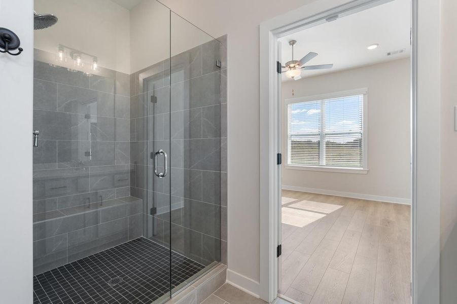 Glass-enclosed shower with grey tile walls and a built-in bench