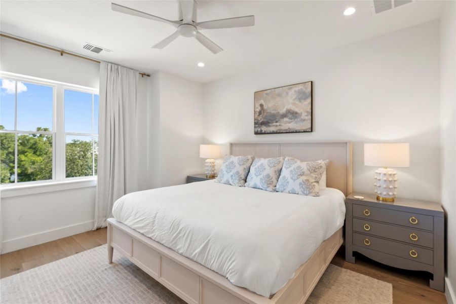 Natural light floods this inviting bedroom, highlighting sleek wood flooring and a contemporary ceiling fan. Natural light floods this inviting bedroom, highlighting sleek wood flooring and a contemporary ceiling fan.