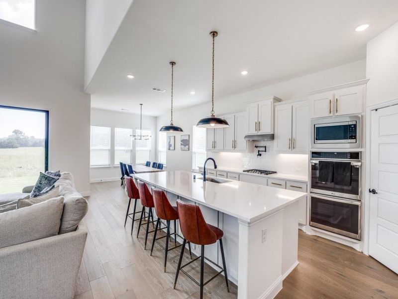Kitchen featuring open floor plan, under cabinet range hood, a sink, light wood-style flooring, and stainless steel appliances Kitchen featuring open floor plan, under cabinet range hood, a sink, light wood-style flooring, and stainless steel appliances