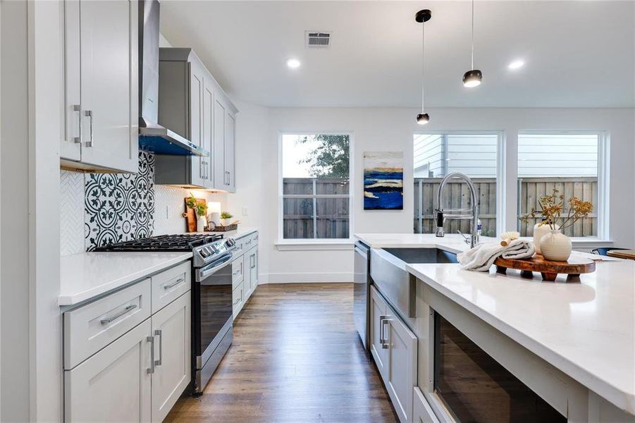 Kitchen featuring dark hardwood / wood-style floors, decorative backsplash, hanging light fixtures, stainless steel appliances, and wall chimney exhaust hood