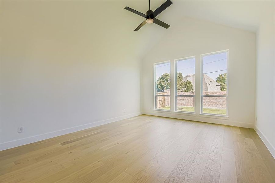 Unfurnished room with light wood finished floors, high vaulted ceiling, and ceiling fan Unfurnished room with light wood finished floors, high vaulted ceiling, and ceiling fan