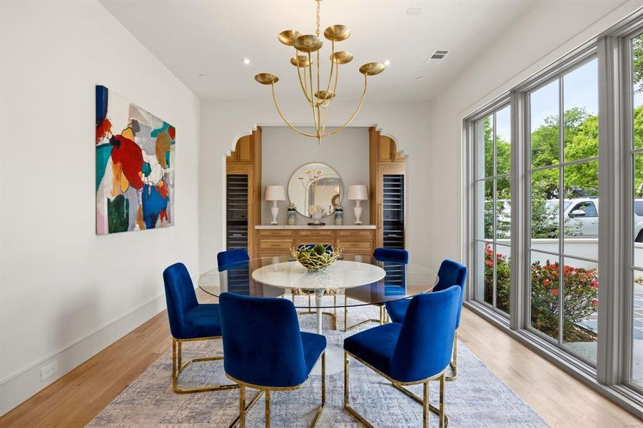 Elegant dining area featuring wood-finish flooring, a contemporary gold-toned chandelier, and a built-in wood cabinet with integrated wine storage Elegant dining area featuring wood-finish flooring, a contemporary gold-toned chandelier, and a built-in wood cabinet with integrated wine storage