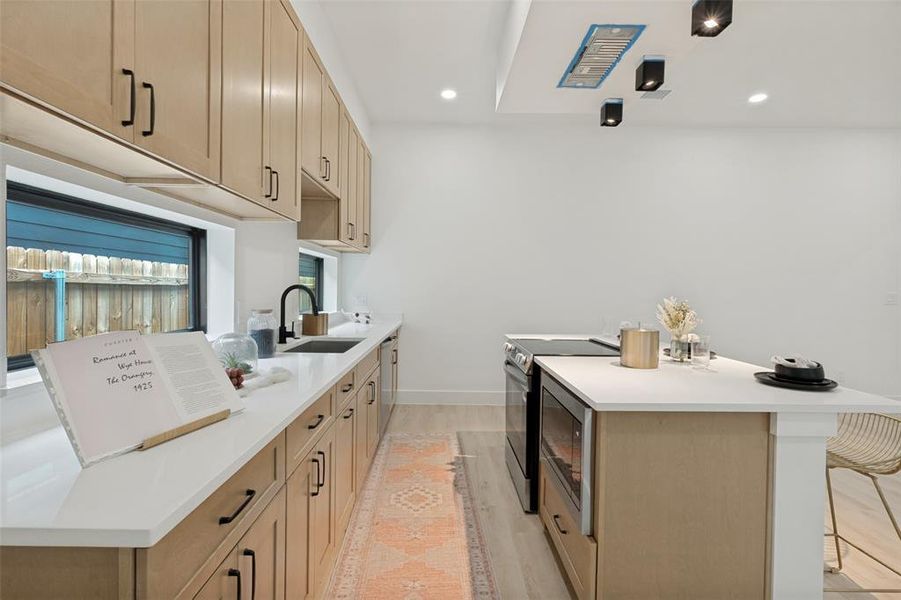 Modern kitchen featuring light wood-finish cabinetry with black hardware, white countertops, and wood-finish flooring