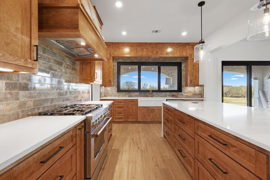 Kitchen with brown cabinets, high end stainless steel range oven, hanging light fixtures, light wood-style flooring, and tasteful backsplash