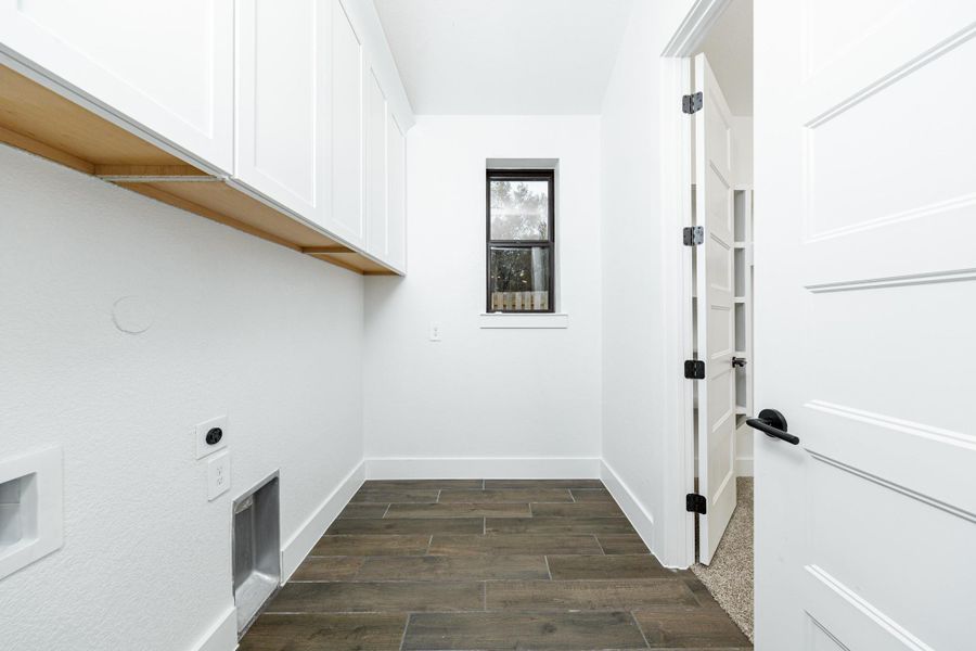 This bright and functional laundry room is conveniently located right off the primary walk-in closet and is ready for your appliances. It features clean white walls, trim, cabinets, window, and tile flooring.