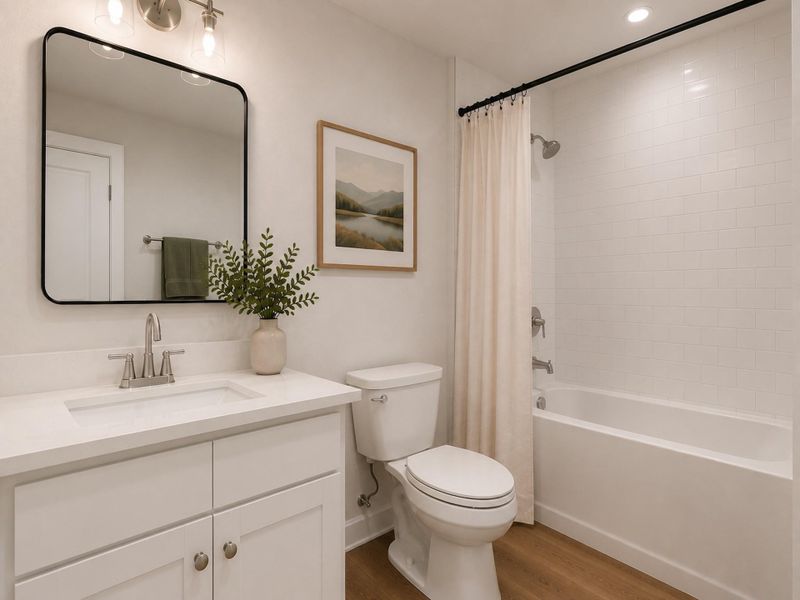 A contemporary full bathroom designed with functionality and elegance in mind. The room features a white shaker vanity with a white quartz countertop, polished chrome plumbing fixtures, and a large black-framed mirror. The tub/shower combination is surrounded by white Cosmopolitan matte subway tile extending to the ceiling, paired with chrome shower trim. Warm Boxwood Wando porcelain flooring, soft greige walls, and understated artwork complete the bright, family-friendly design.