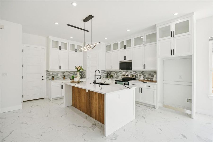 Kitchen with glass insert cabinets, white cabinetry, a center island with sink, light marble finish flooring, and recessed lighting