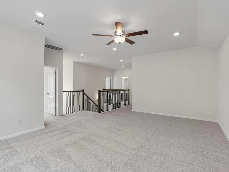 A spacious upstairs landing with vaulted ceilings, featuring neutral carpeting and recessed lighting.
