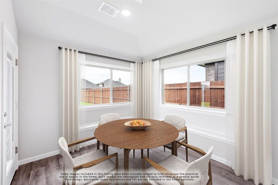 Bright dining area with round wood table, four chairs, and two large windows with cream curtains