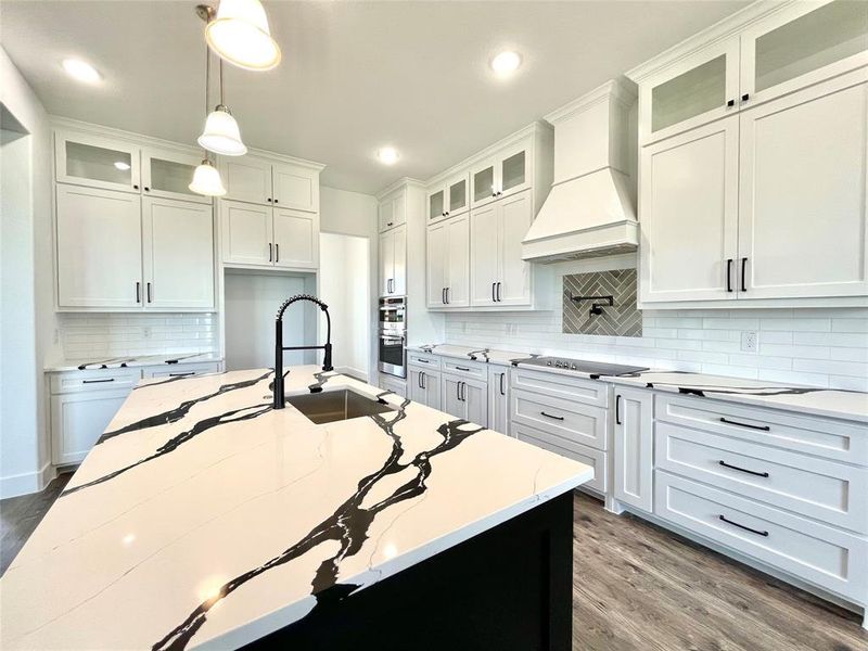 Kitchen with custom exhaust hood, wood finished floors, a sink, decorative backsplash, and black electric stovetop Kitchen with custom exhaust hood, wood finished floors, a sink, decorative backsplash, and black electric stovetop
