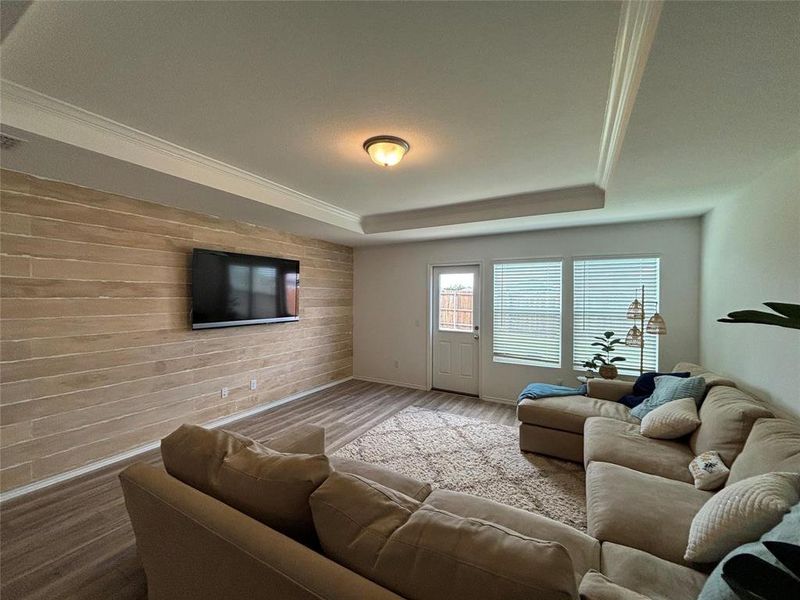Living room featuring wood walls, a raised ceiling, wood finished floors, and ornamental molding