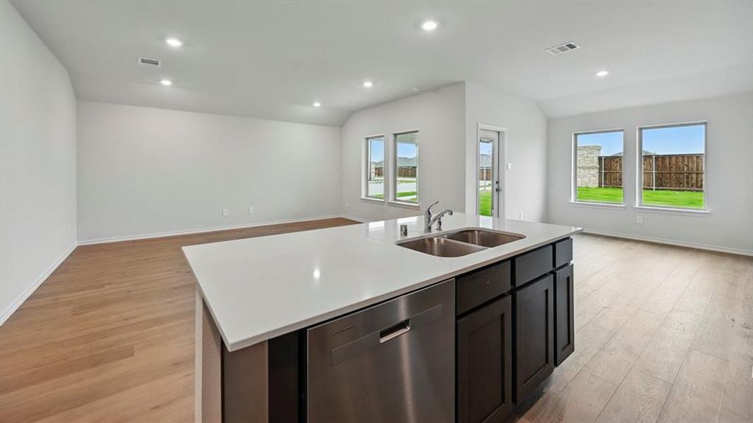 Kitchen with open floor plan, stainless steel dishwasher, vaulted ceiling, a center island with sink, and light wood-type flooring