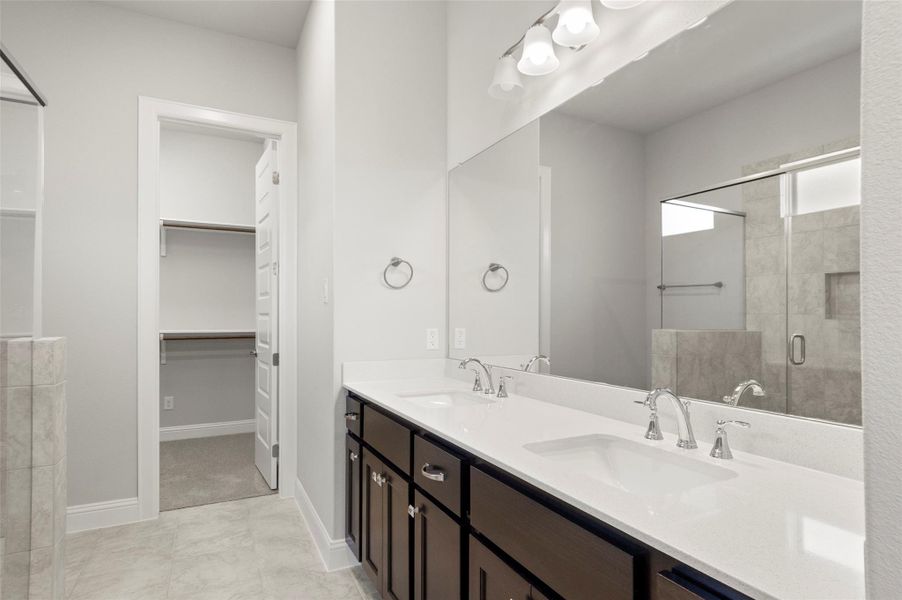 Full bath with a stall shower, double vanity, and a walk in closet