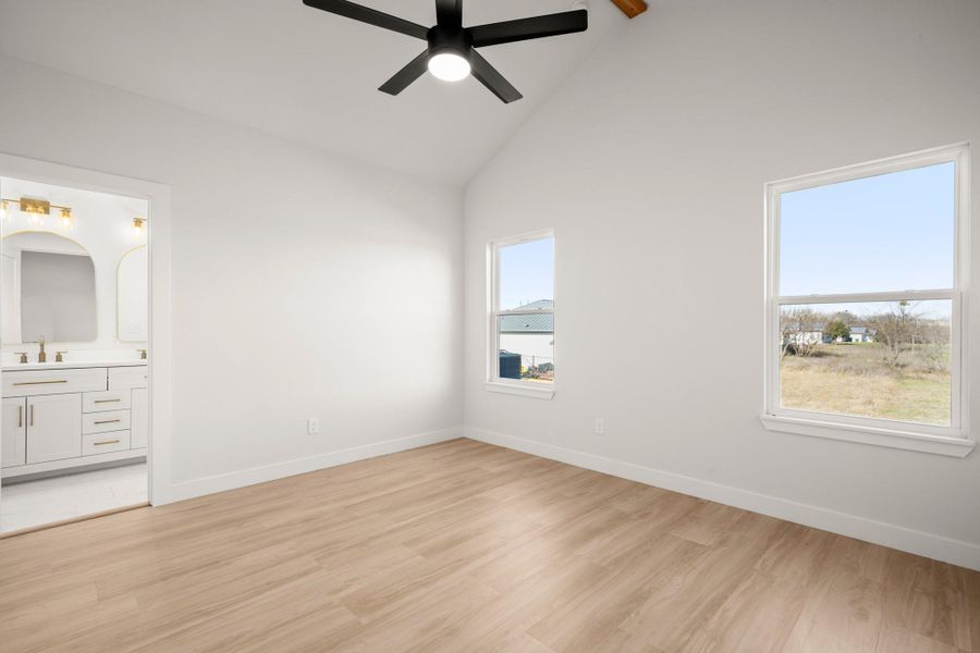 Unfurnished bedroom featuring light wood-style flooring, vaulted ceiling, ceiling fan, and ensuite bathroom