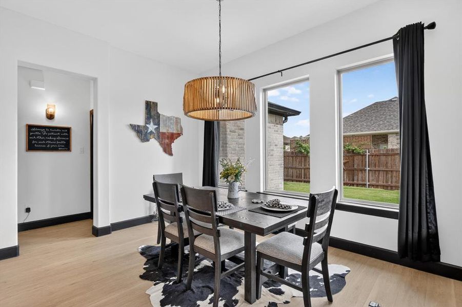 Dining area featuring wood-finish flooring, a contemporary drum pendant light, and two large windows with black trim
