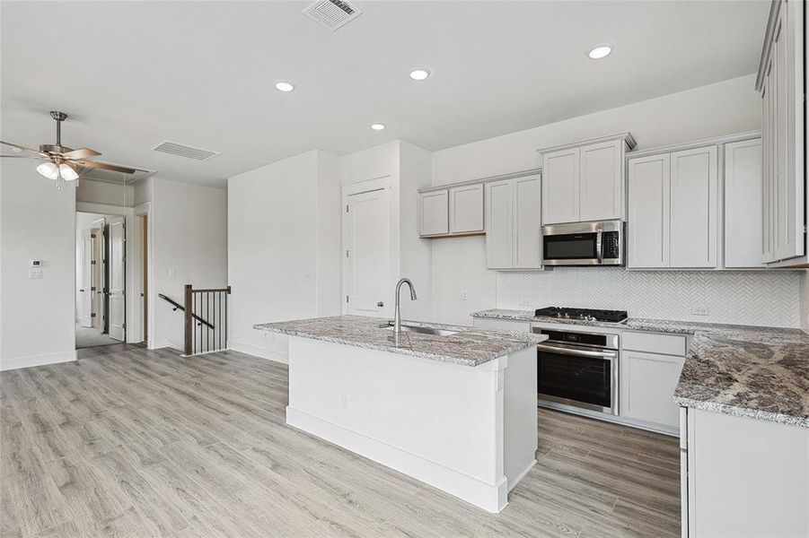 Kitchen with appliances with stainless steel finishes, tasteful backsplash, sink, an island with sink, and ceiling fan