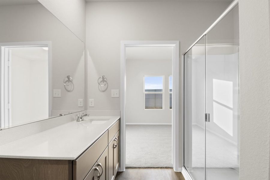 Image of a bathroom with a large mirror and white vanity with a walk-in shower and a door leading to the primary bedroom