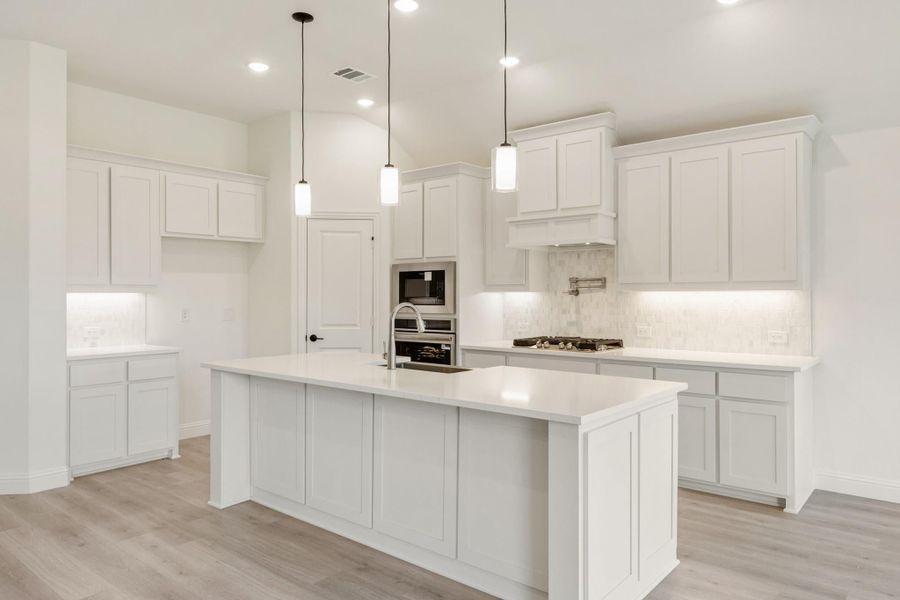 White kitchen with large center island, pendant lights, stainless appliances, and light wood floors White kitchen with large center island, pendant lights, stainless appliances, and light wood floors