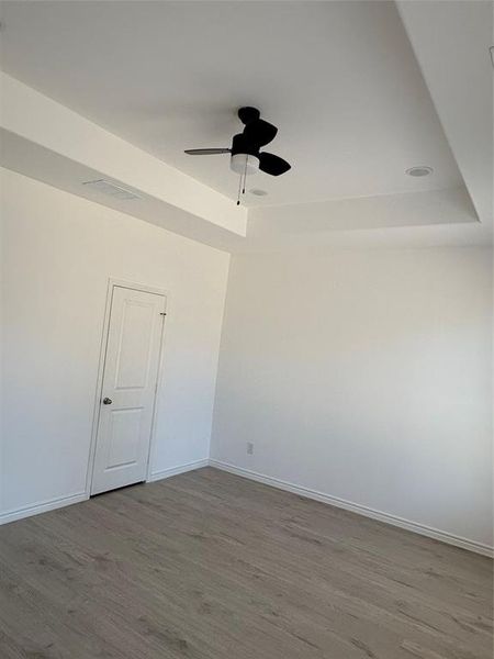 Empty room with wood finished floors, a raised ceiling, and a ceiling fan