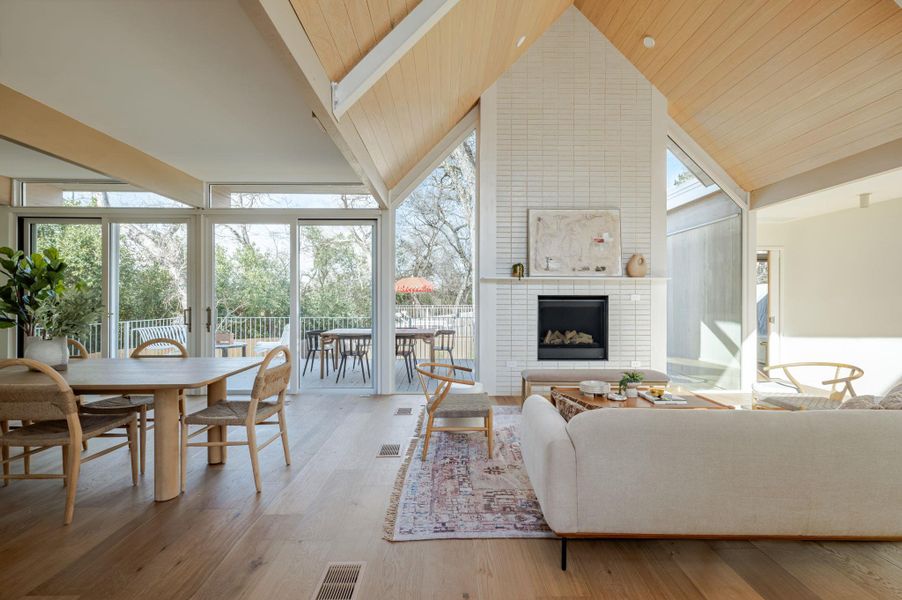 Living area with a brick fireplace, light wood-style floors, and a high wood beamed ceiling