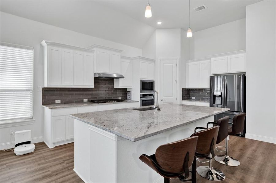 Kitchen featuring white cabinetry, light stone countertops, a breakfast bar area, backsplash, and stainless steel appliances