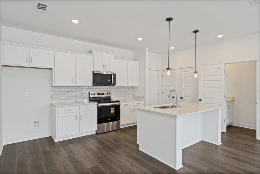 Kitchen featuring wood-finish flooring, white cabinetry, a white subway tile backsplash, stainless steel appliances, and an island with a stainless steel sink Kitchen featuring wood-finish flooring, white cabinetry, a white subway tile backsplash, stainless steel appliances, and an island with a stainless steel sink