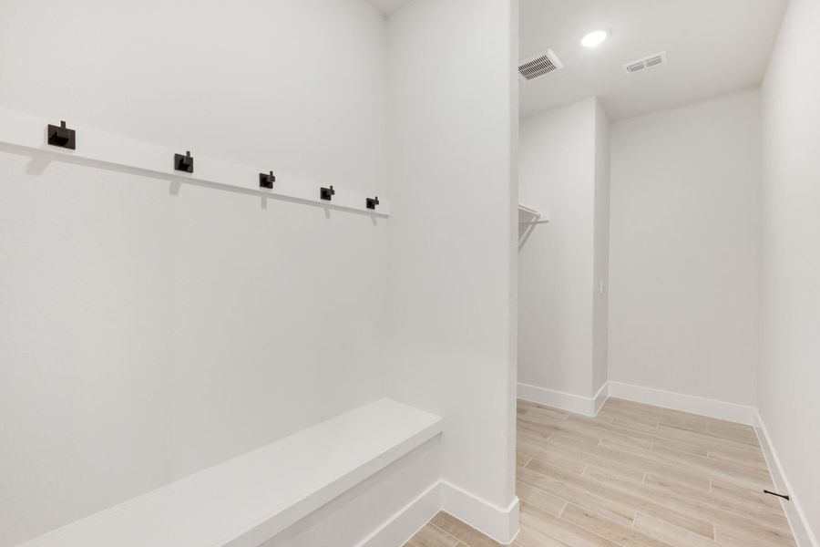 Mudroom with built-in bench, black wall hooks, and light wood-look tile floors leading to a closet area.