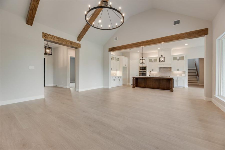 Unfurnished living room with a chandelier, light wood-type flooring, stairway, recessed lighting, and high vaulted ceiling
