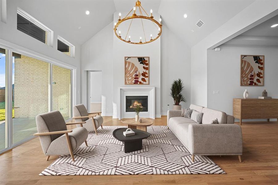 Living area with high vaulted ceiling, a chandelier, light wood-style flooring, a glass covered fireplace, and recessed lighting Living area with high vaulted ceiling, a chandelier, light wood-style flooring, a glass covered fireplace, and recessed lighting