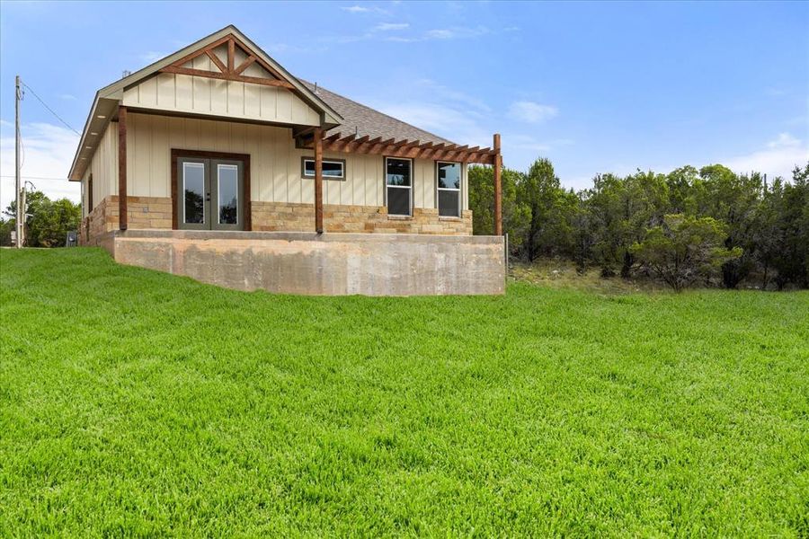 Back of house featuring a lawn, stone siding, board and batten siding, french doors, and a shingled roof Back of house featuring a lawn, stone siding, board and batten siding, french doors, and a shingled roof