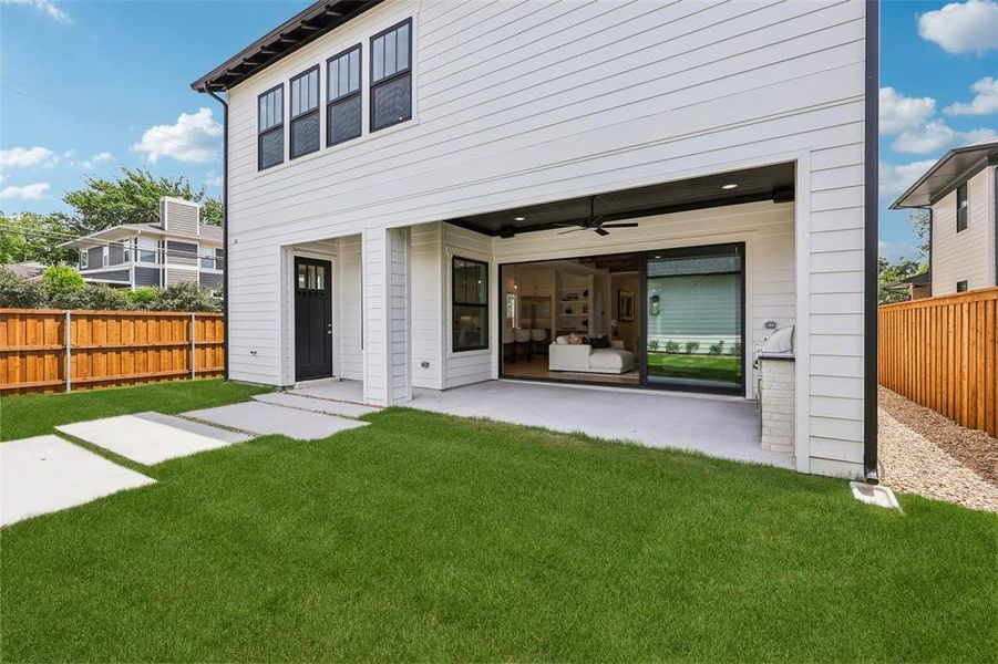 Expansive backyard featuring a covered patio, built-in outdoor cooking station, and a manicured lawn with concrete stepping stones