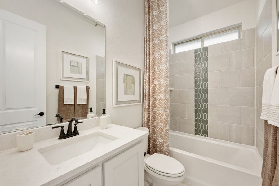 Bathroom with white vanity, tub-shower combo with tile surround, and patterned curtain