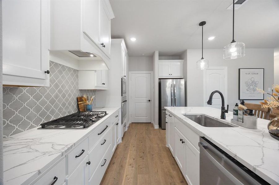 Kitchen with light stone counters, tasteful backsplash, white cabinetry, appliances with stainless steel finishes, and light wood-type flooring