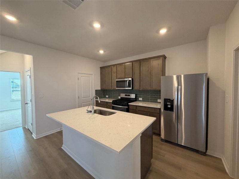 Kitchen with appliances with stainless steel finishes, light stone countertops, backsplash, a center island with sink, and dark brown cabinets