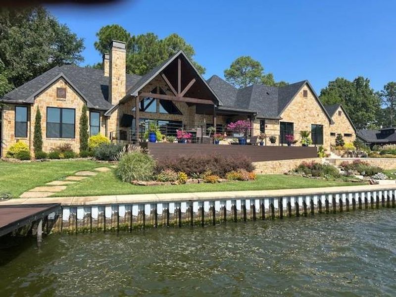 Rear view of property with stone siding, a patio area, a chimney, and a water view