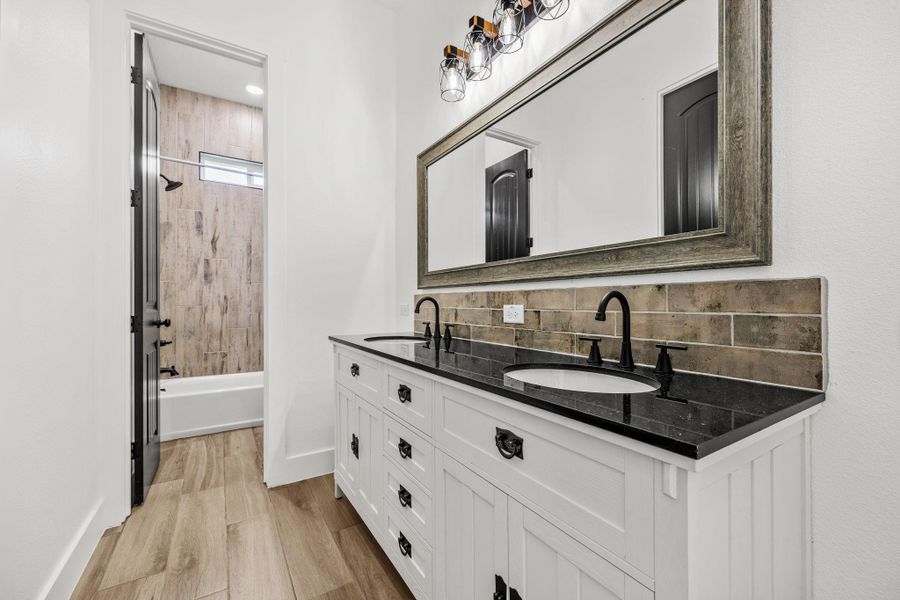 Full bath featuring double vanity, light wood-style flooring,  shower combination, and tasteful backsplash