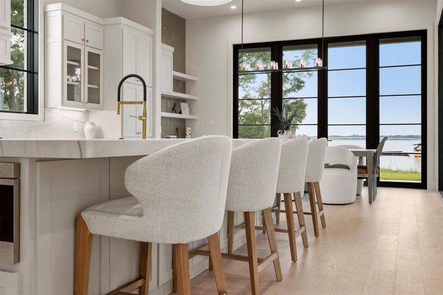 Kitchen featuring a water view, white cabinets, light wood-type flooring, glass insert cabinets, and a kitchen breakfast bar Kitchen featuring a water view, white cabinets, light wood-type flooring, glass insert cabinets, and a kitchen breakfast bar