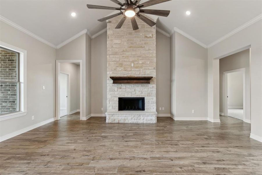 Unfurnished living room featuring ceiling fan, a stone fireplace, lofted ceiling, and crown molding