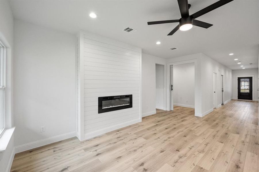 Unfurnished living room with a large fireplace, light wood finished floors, visible vents, baseboards, and recessed lighting