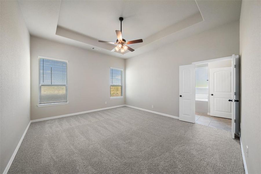 Empty room featuring a raised ceiling, carpet floors, and ceiling fan Empty room featuring a raised ceiling, carpet floors, and ceiling fan