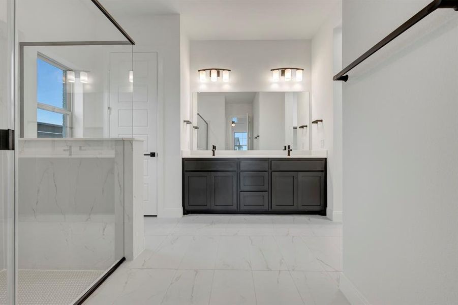 Bathroom featuring double vanity, light marble finish floors, and a marble finish shower