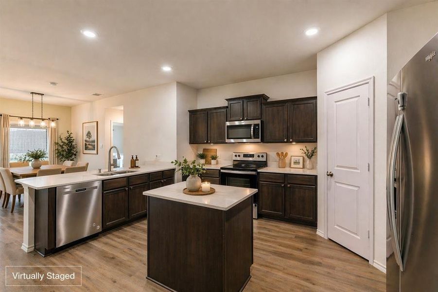 Modern kitchen featuring dark wood cabinetry, white countertops, stainless steel appliances, and wood-finish flooring Modern kitchen featuring dark wood cabinetry, white countertops, stainless steel appliances, and wood-finish flooring