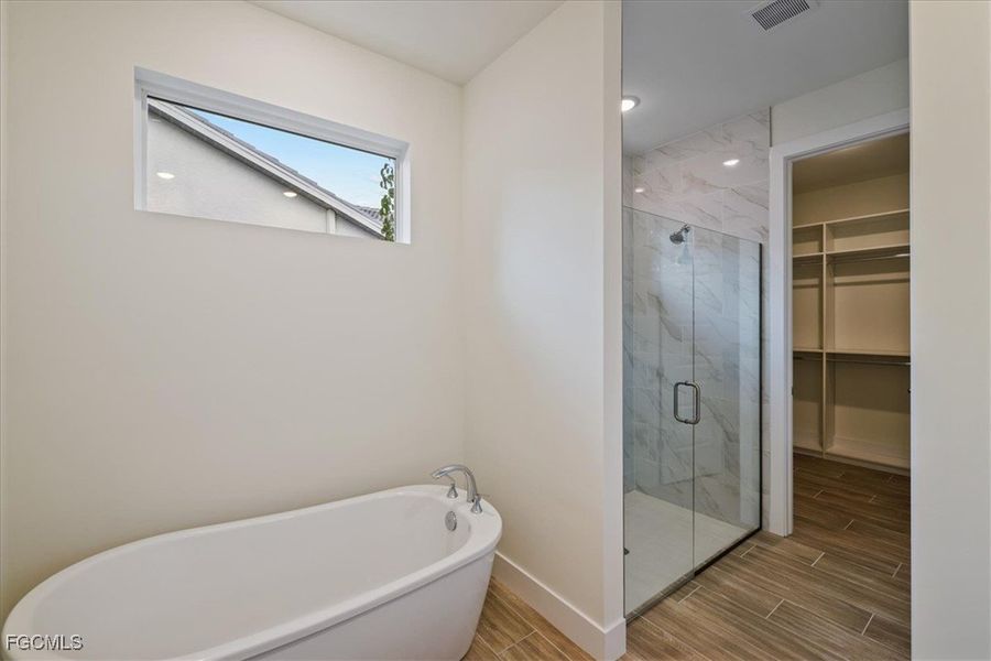 Full bath with wood tiled floors, a freestanding tub, a marble finish shower, and a spacious closet