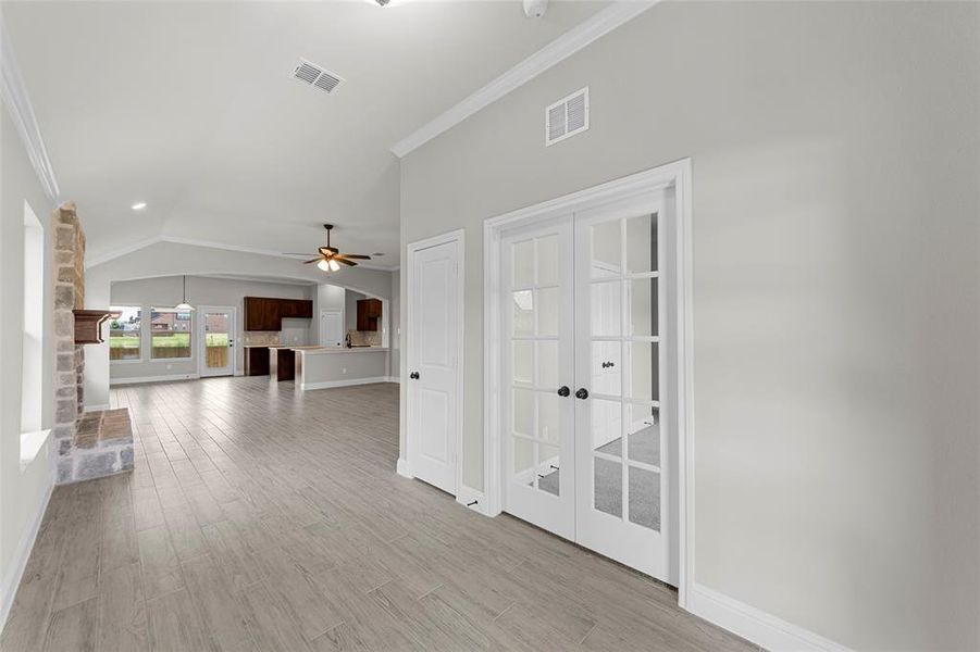 Unfurnished living room featuring ornamental molding, french doors, lofted ceiling, light wood-style flooring, and a ceiling fan