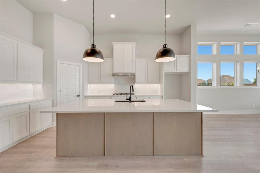 Expansive kitchen island with a light-toned base, complemented by white cabinetry, light countertops, and a white tile backsplash