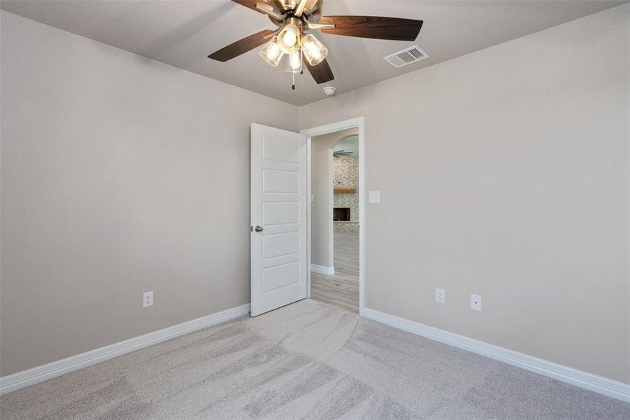 Carpeted room featuring a ceiling fan with light fixture, light gray walls, white trim, and a five-panel interior door Carpeted room featuring a ceiling fan with light fixture, light gray walls, white trim, and a five-panel interior door
